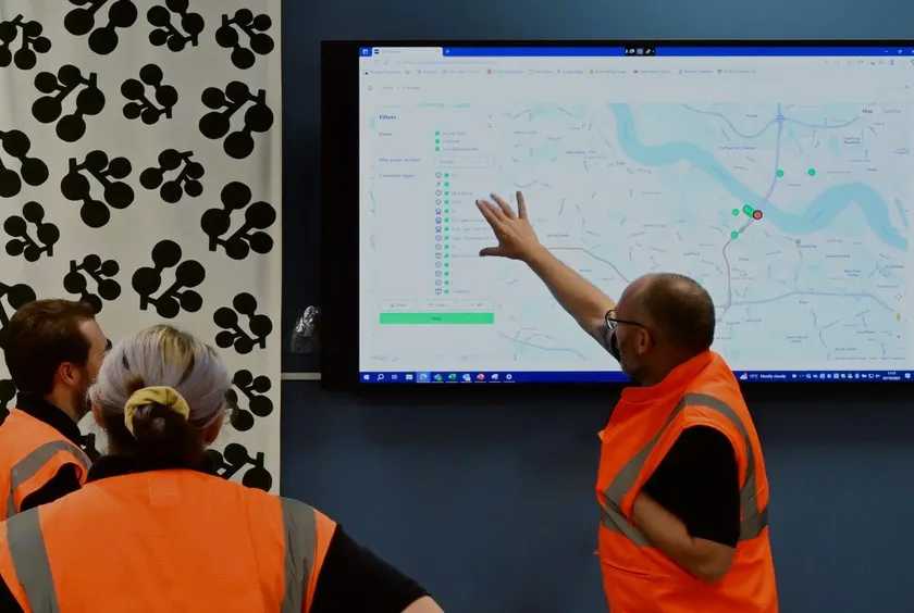 A team in hi-vis vests gathered around a screen showing the FPS Operate live map